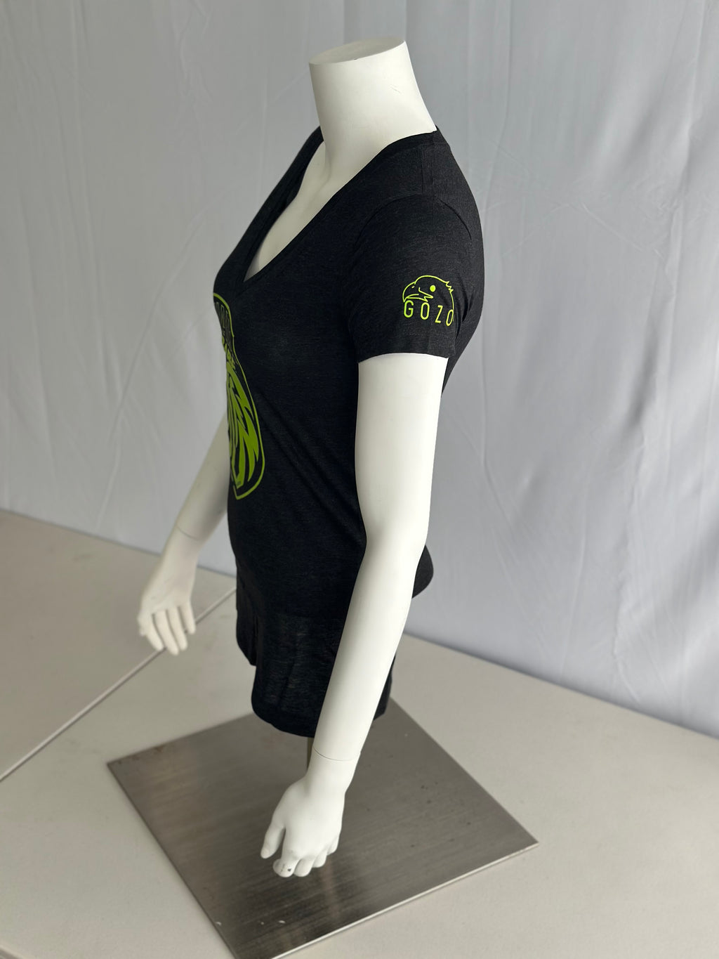 A dark gray short-sleeve V-neck T-shirt displayed on a white mannequin torso and arm. The shirt has a large lime green graphic on the front and a small lime green logo patch on the left sleeve.