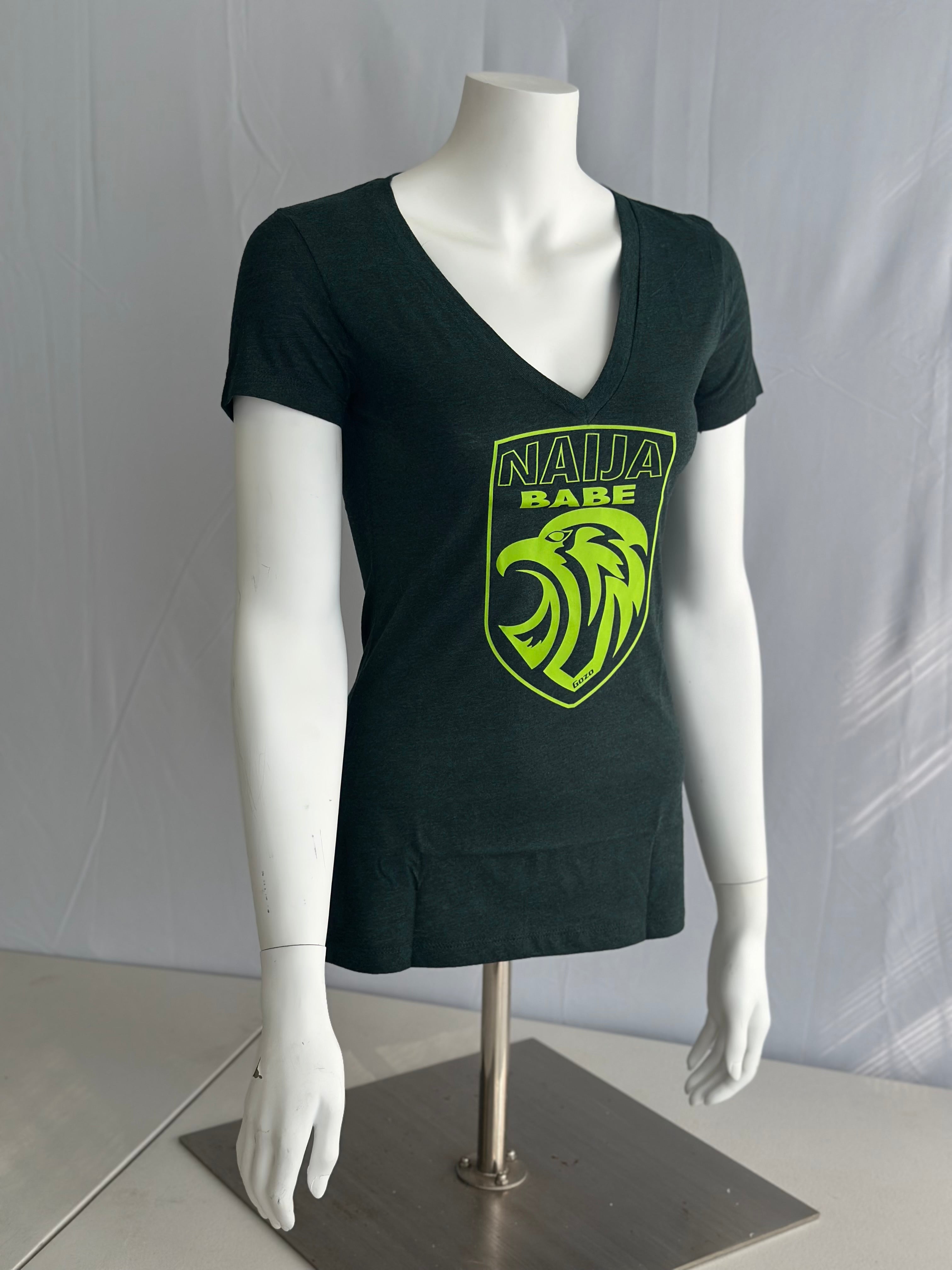 A dark green short-sleeve V-neck t-shirt displayed on a white mannequin torso. The shirt features a bright lime green shield logo on the chest with the text 'NAIJA BABE' and a stylized eagle head.