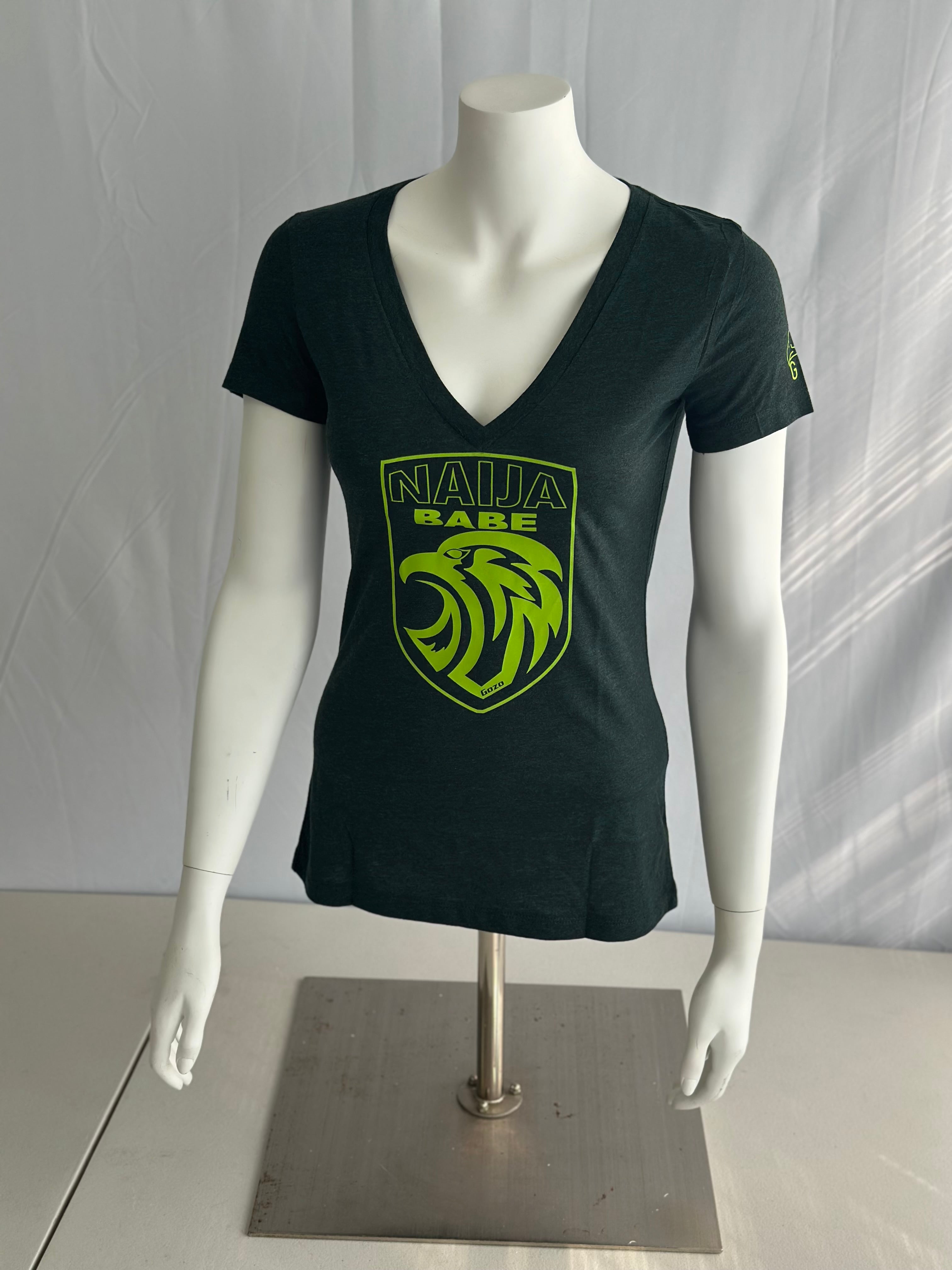 A dark green short-sleeve V-neck t-shirt displayed on a white mannequin torso with arms. The shirt features a bright lime green shield graphic on the chest with a stylized lion head and the text 'NAIJA BABE' in lime green.